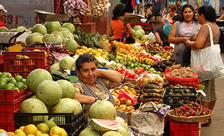 Verkauferin inmitten ihres Marktstandes mit Obst und Gemüse.